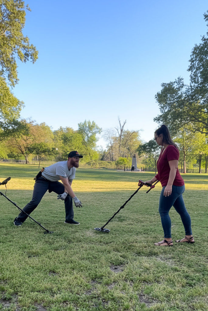 Two people using metal detectors in a park on a sunny day